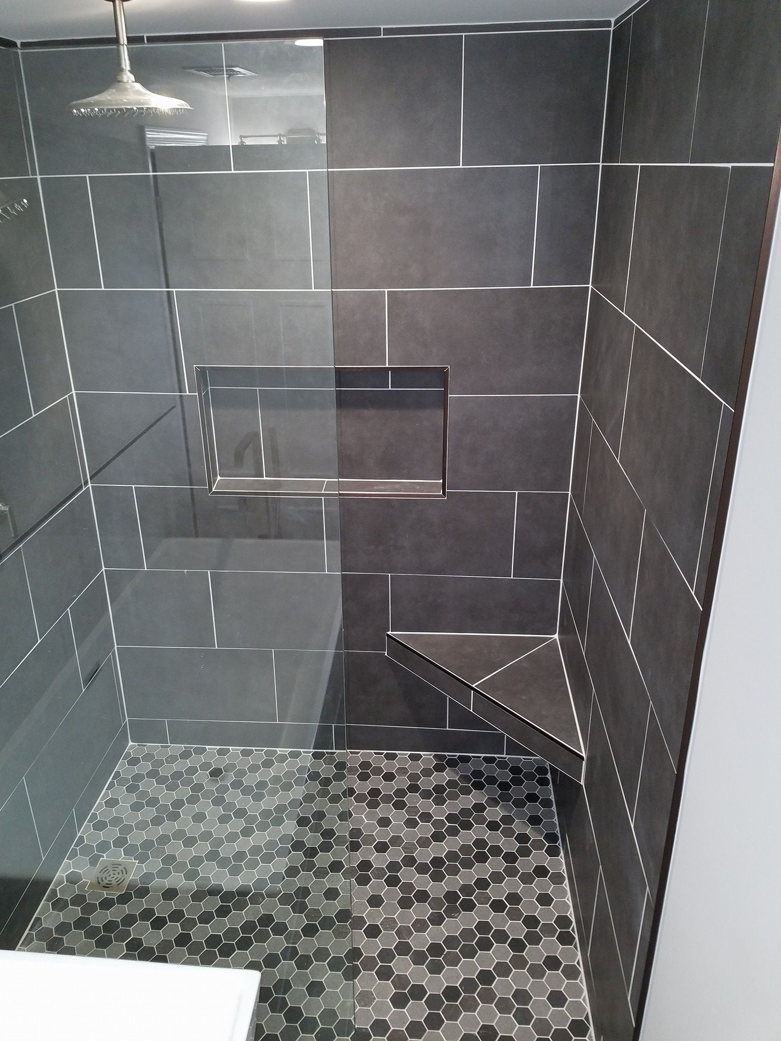 Modern shower with dark gray tiles, glass, and geometric floor.