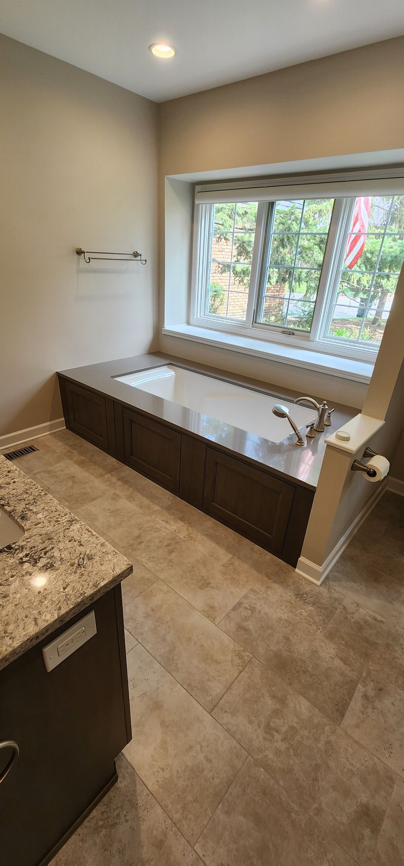 Bathroom with built-in tub under a window. Dark brown cabinetry, beige walls, and granite countertop.