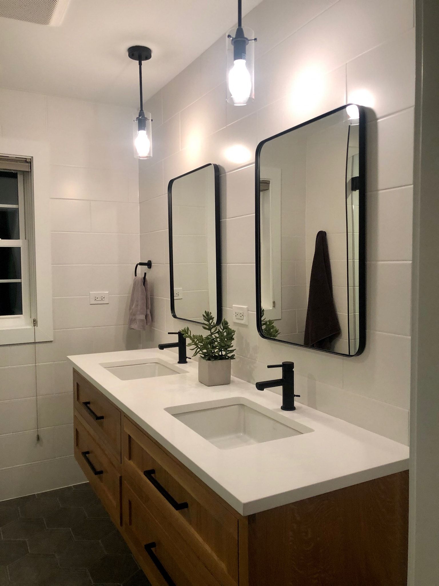 Modern bathroom with floating wooden vanity, white countertops, black fixtures, two mirrors, and pendant lights.