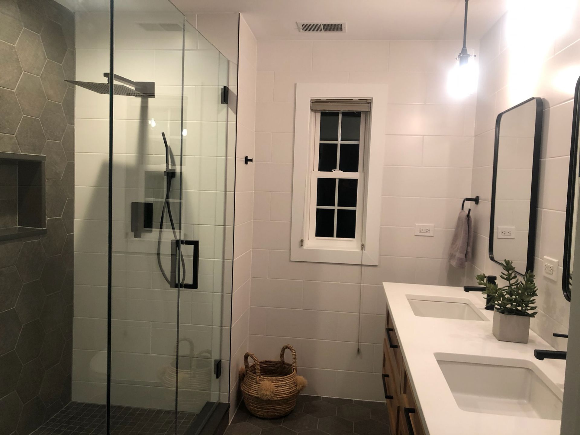Bathroom with shower, double vanity, and small window; gray and white tile, wooden vanity.