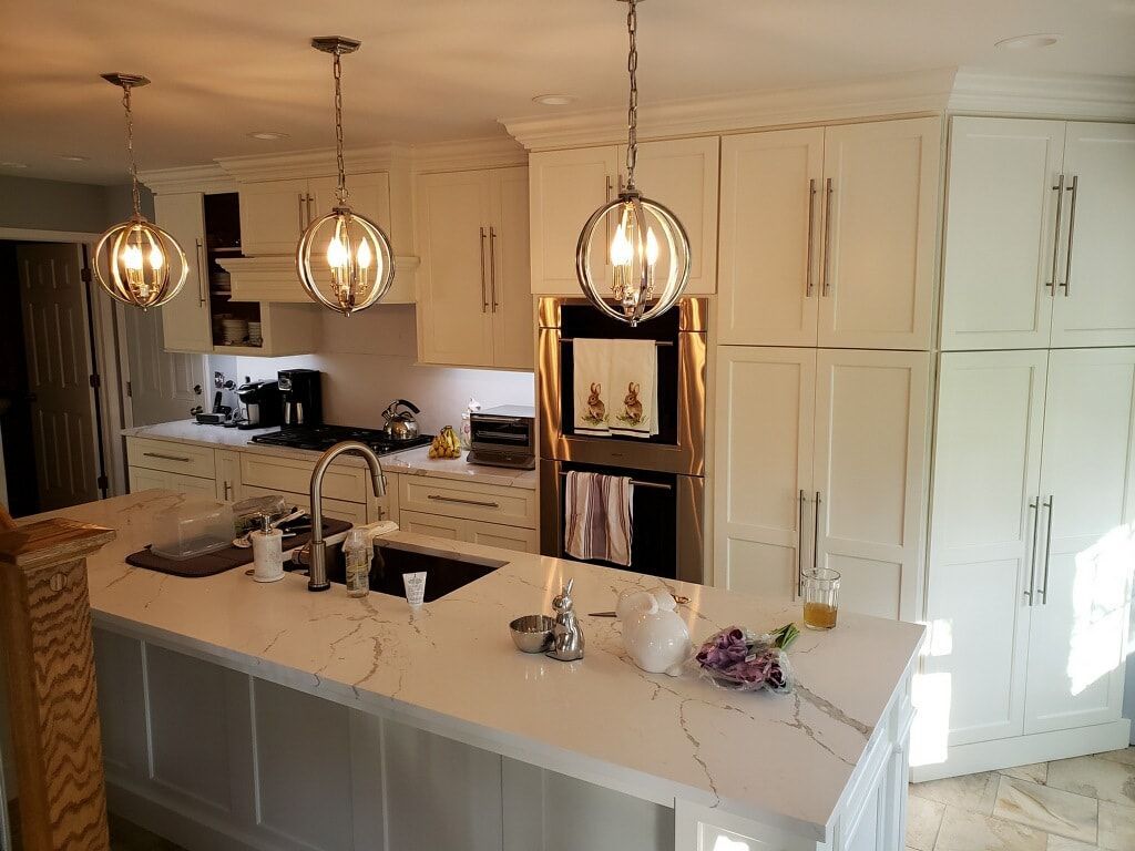 White kitchen with island, pendant lights, stainless steel appliances, and white cabinets.