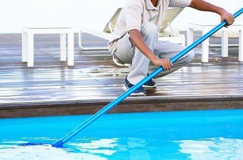 Man using pool skimmer to clean a pool