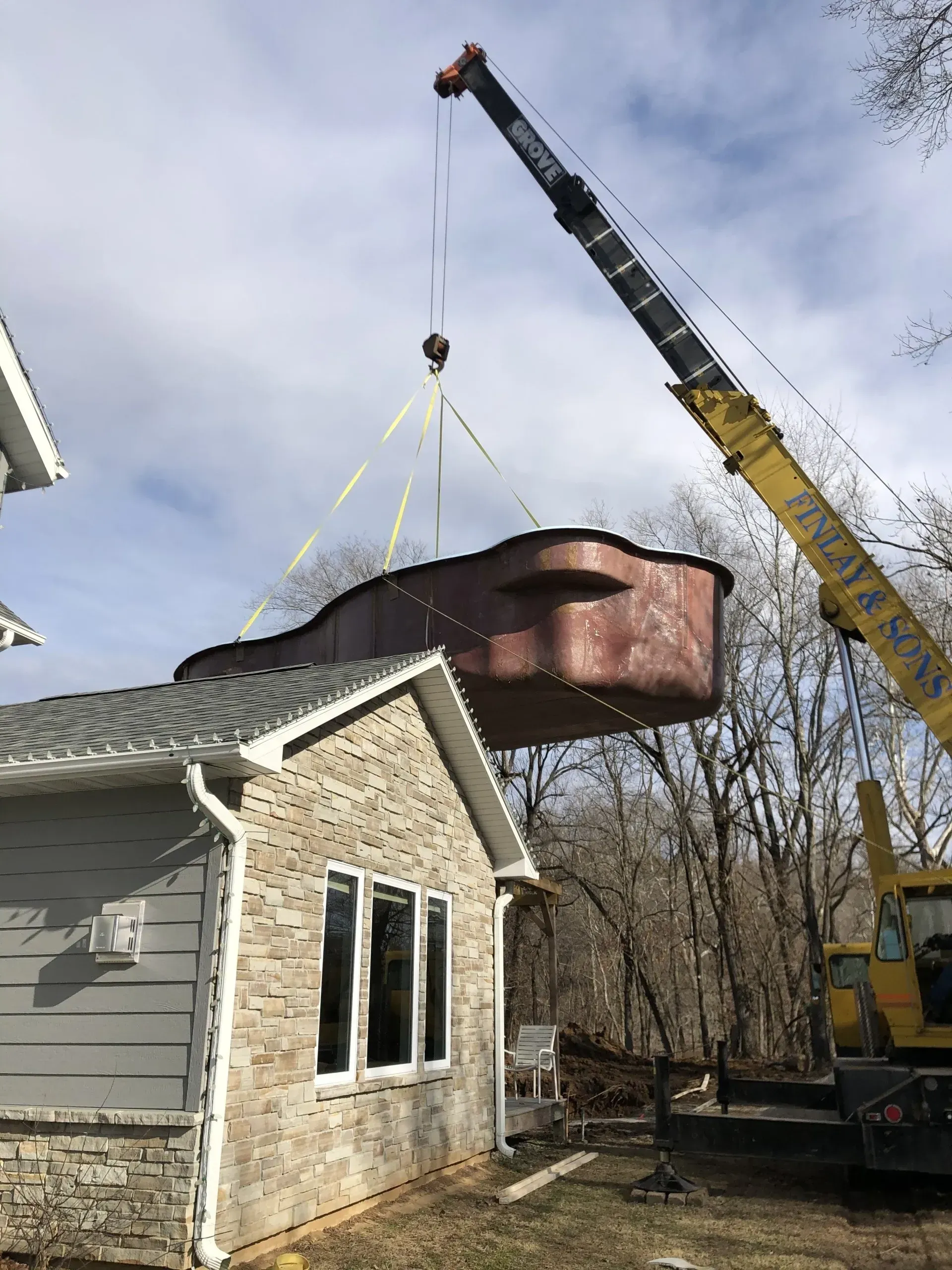a pool being lowered into the backyard of a home by a crane