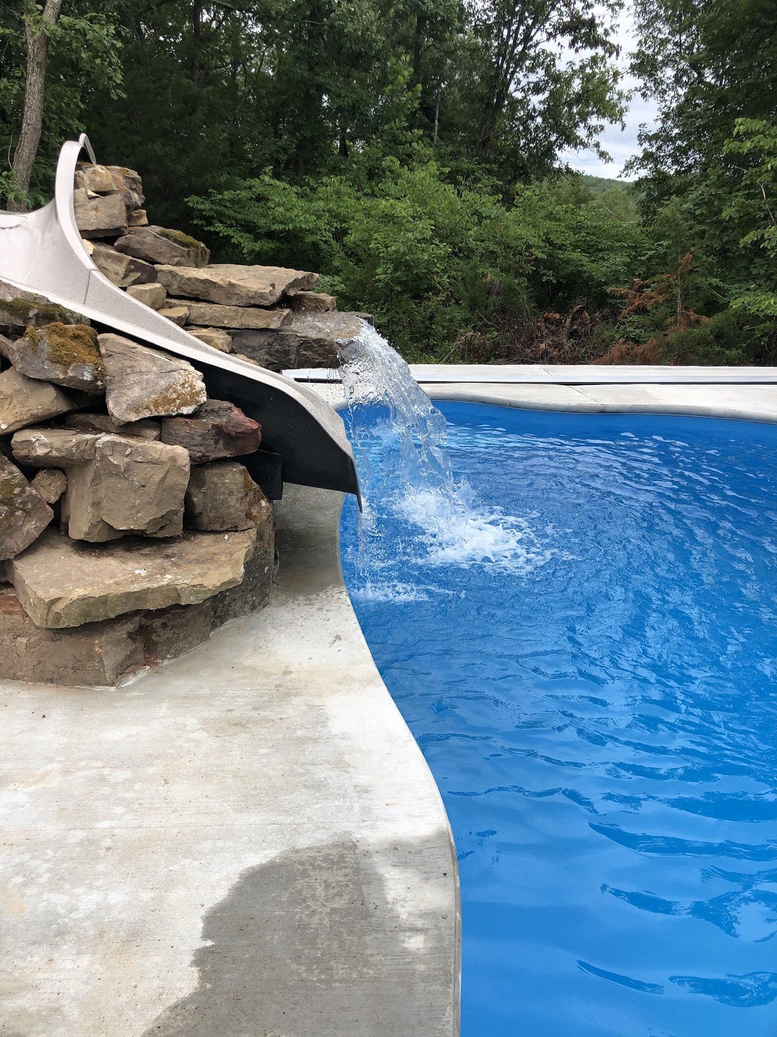 A pool with a stone waterfall and slide. Clear water flowing into the blue pool on a sunny day.