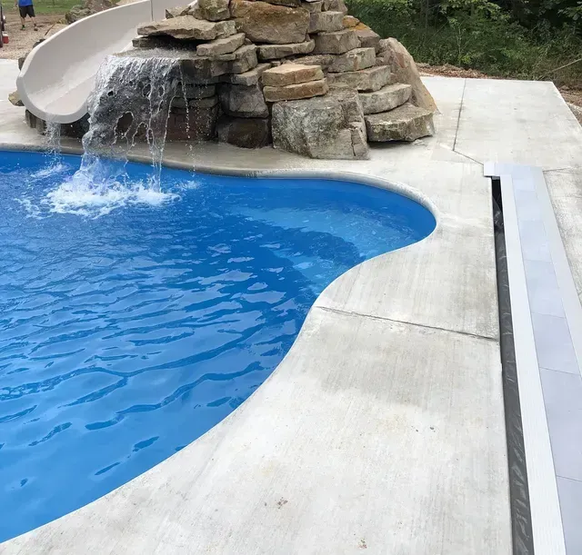 The corner of a pool with a slide and waterfall feature
