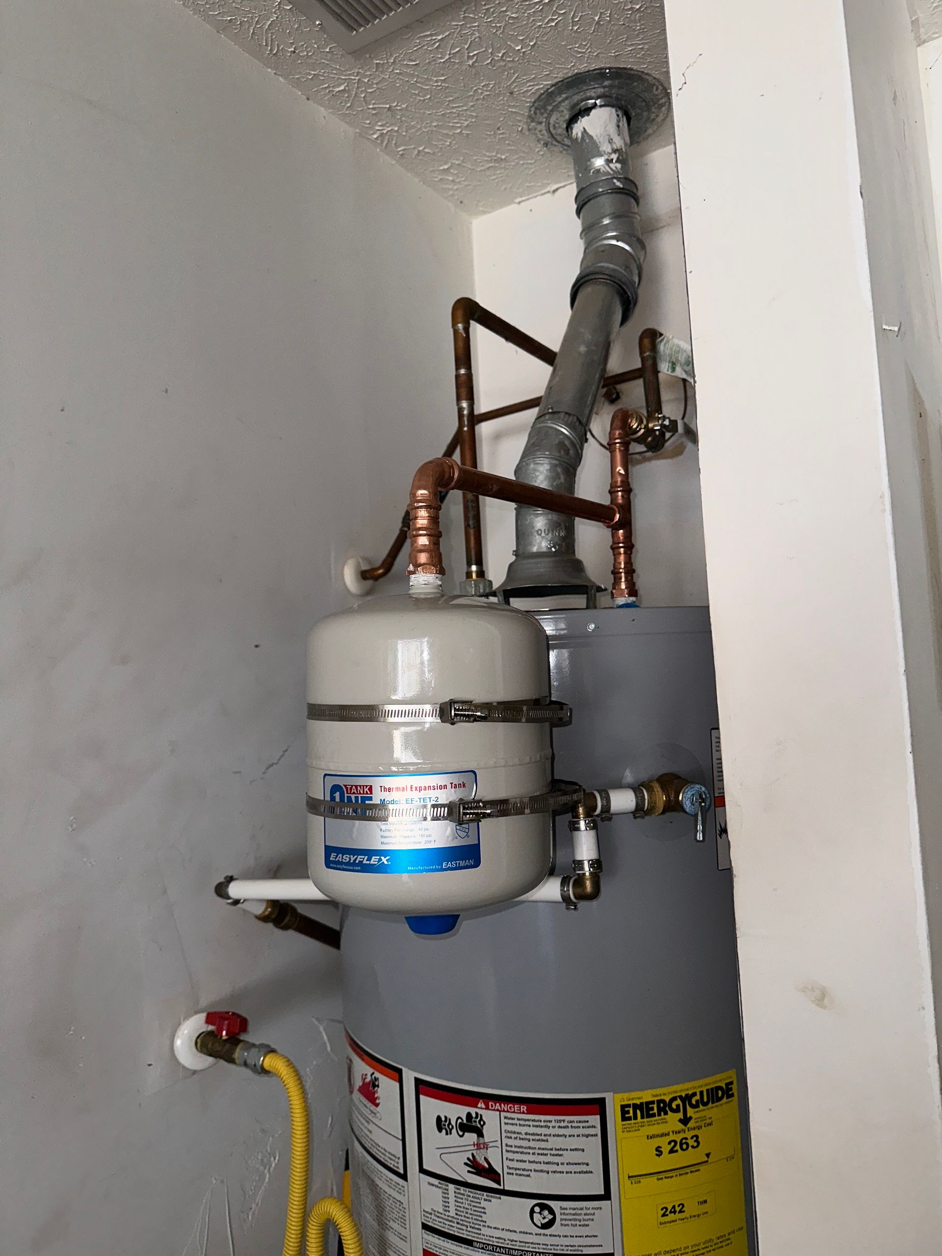 Water heater with connected expansion tank and vent pipe in a white utility room.