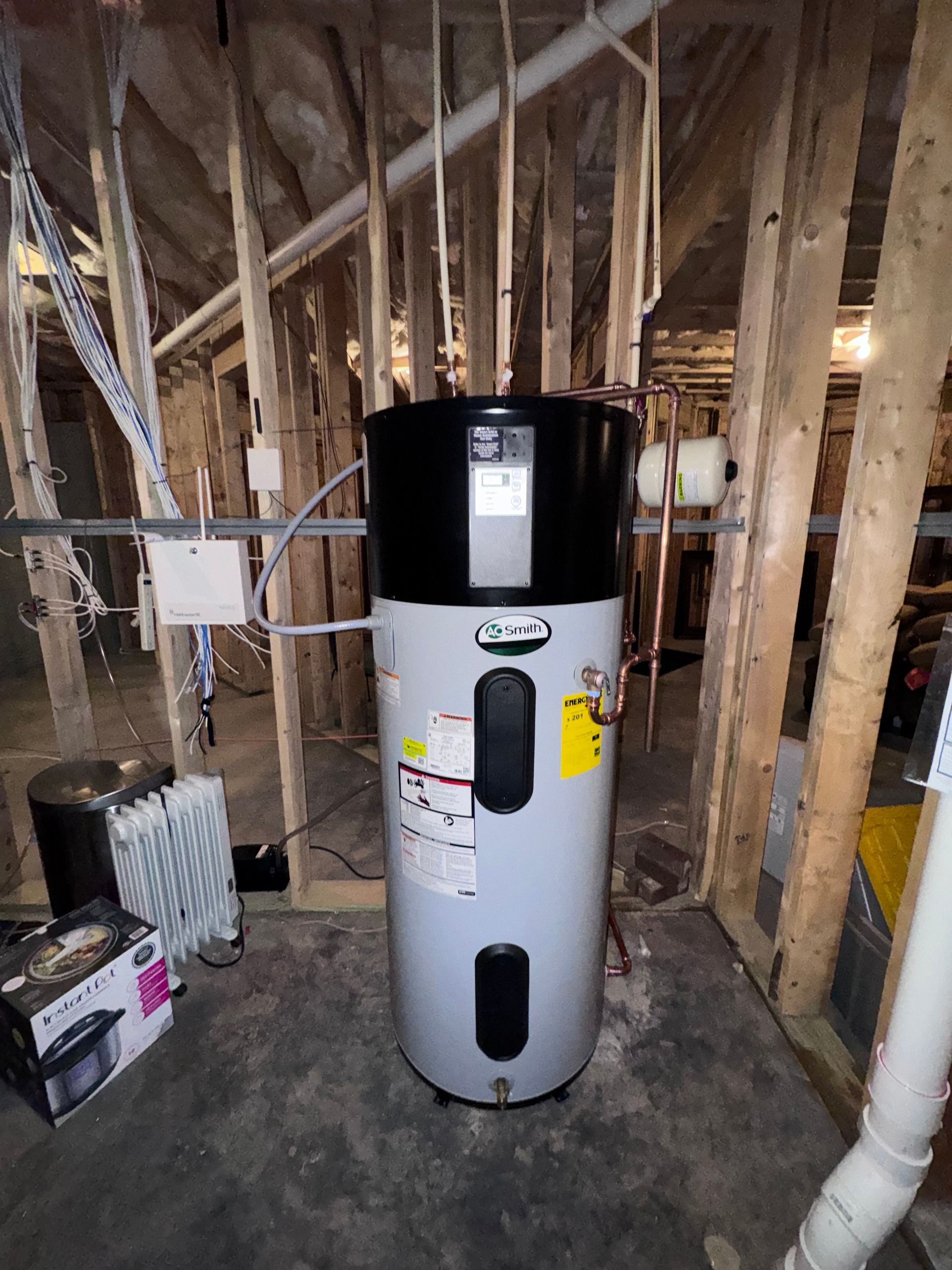 A tall gray and black heat pump water heater sits in a basement.