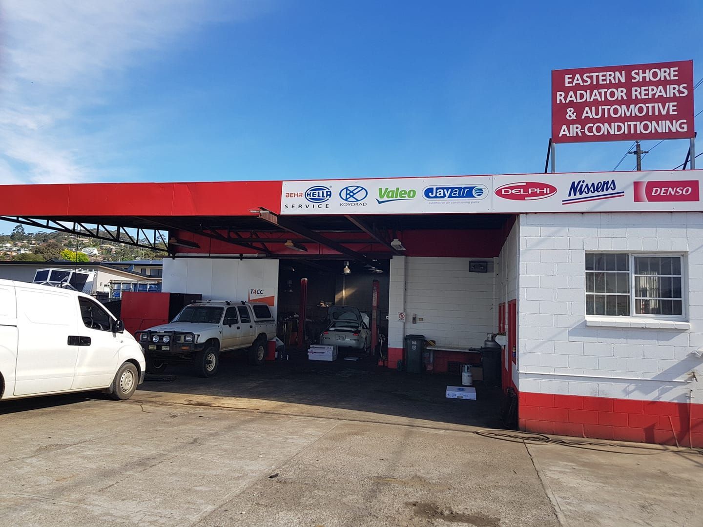 A white van is parked in front of a car repair shop.