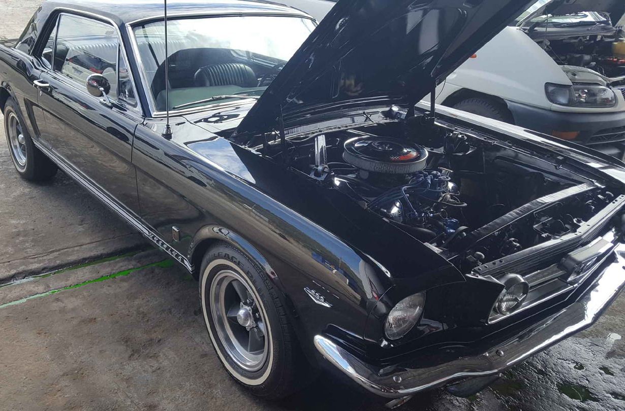 A black car with the hood up is parked in a parking lot.