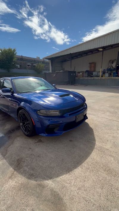A blue dodge charger is parked in a parking lot in front of a building.