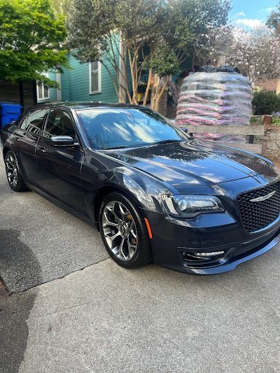 A black chrysler 300 is parked in a driveway in front of a house.