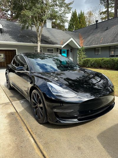 A black tesla model 3 is parked in front of a house.