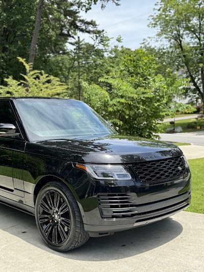A black range rover is parked in a driveway next to trees.