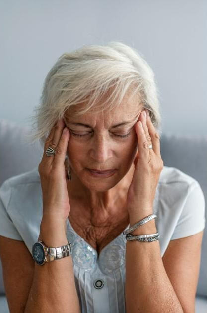 An individual with their eyes closed and hands pressed to their temples, appearing to experience a headache or stress.
