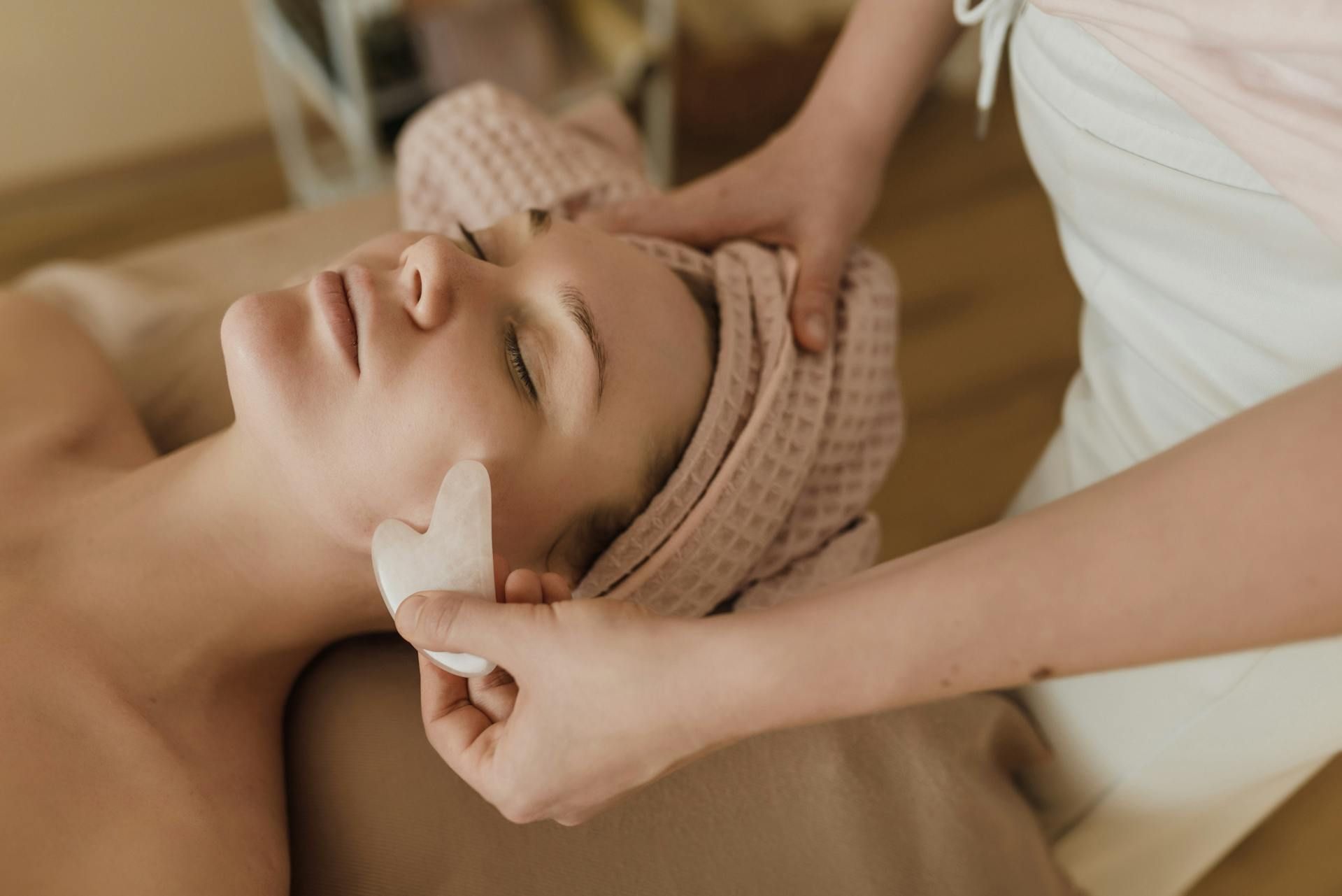 A person receives a gua sha facial massage from a practitioner in a spa setting.