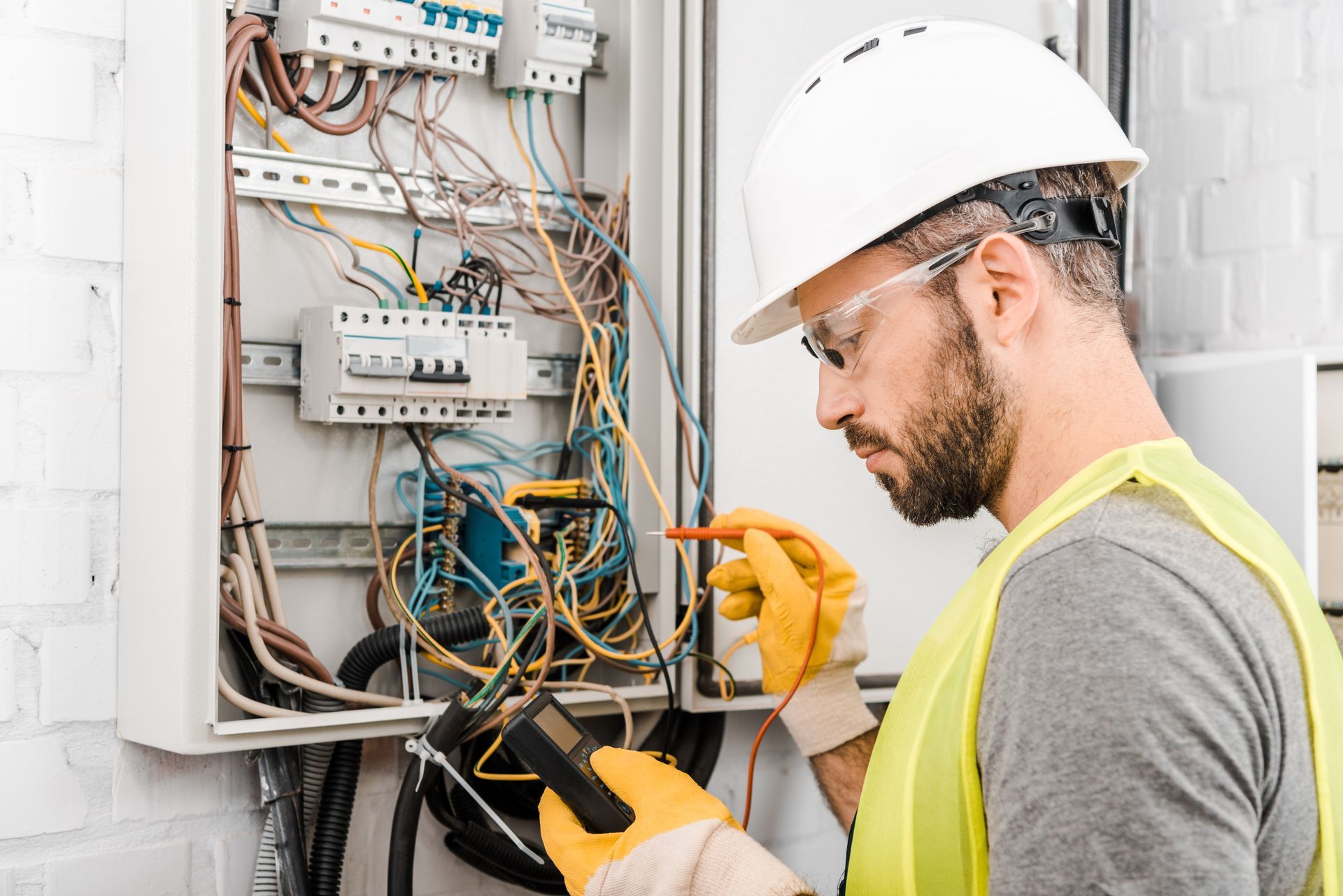 An electrician testing wires inside an open electrical panel using a meter and insulated tools.