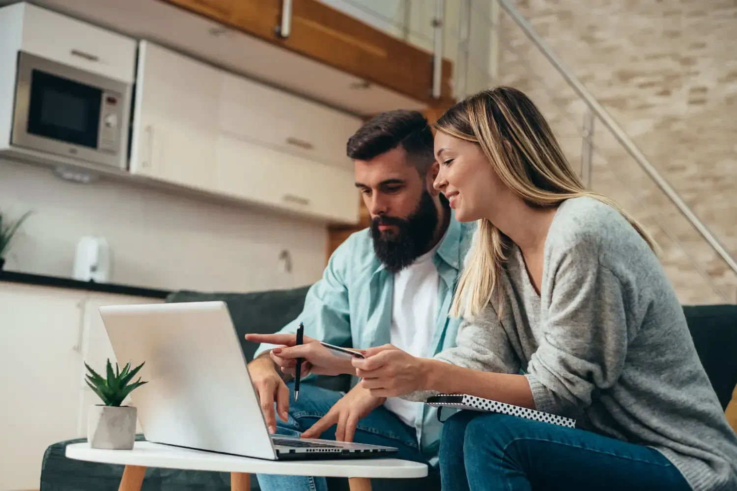 A man and a woman are sitting on a couch looking at a laptop.