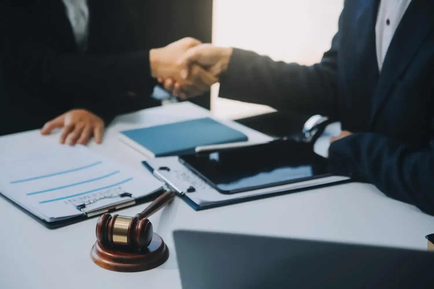 Two men are shaking hands over a table with papers and a judge 's gavel.