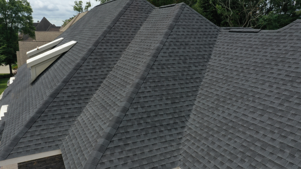 Gray shingled roof with multiple ridges and roof vents on a suburban house