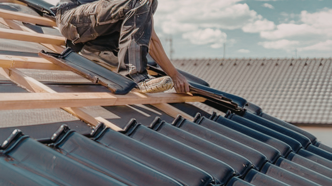 Worker installing blue roof shingles on a house roof