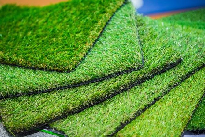 Stacked green artificial turf mats with dark backing and folded edges.