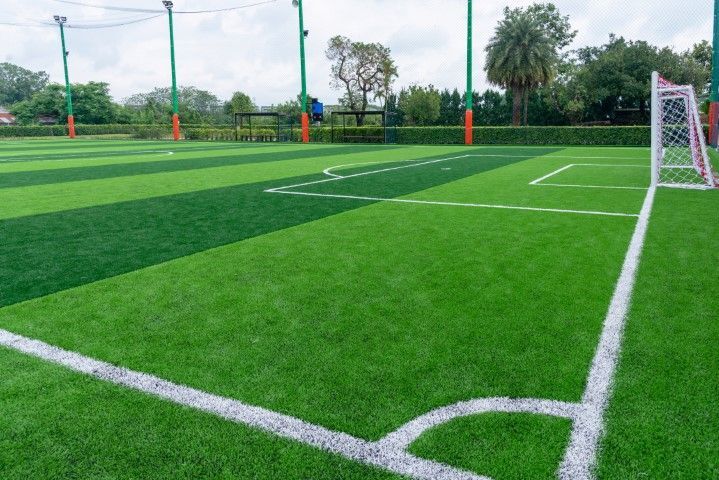 Empty soccer field with bright green turf, white markings, and a goal under a cloudy sky
