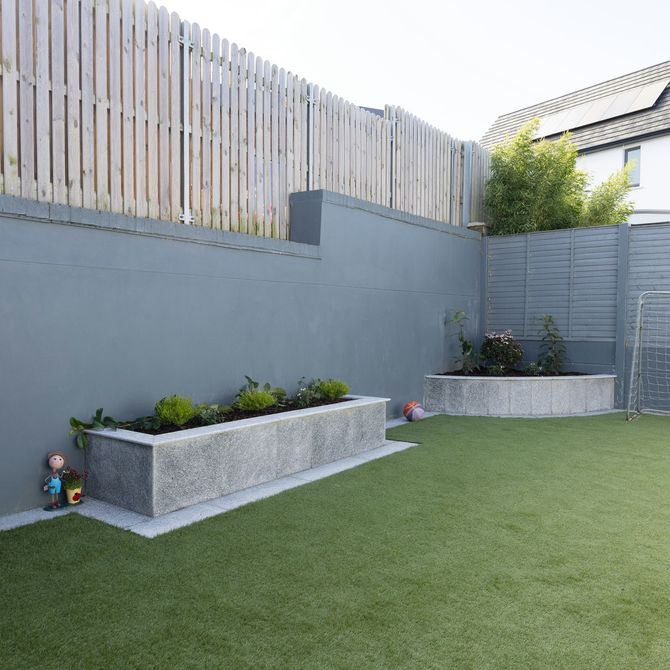 Modern backyard with artificial grass, raised garden beds, gray walls, and wooden fencing.