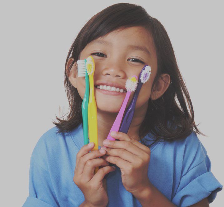 kid smiling holding multiple toothbrushes
