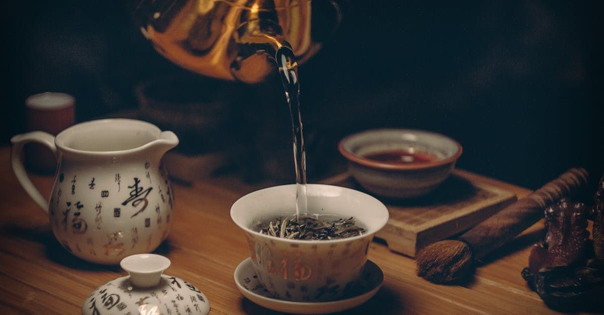 A person is pouring tea into a cup on a wooden table.