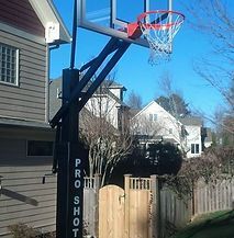 A basketball hoop is sitting in front of a house next to a wooden fence.