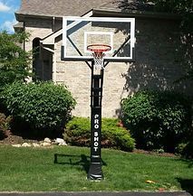 A basketball hoop is sitting in the grass in front of a house.