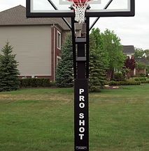 A basketball hoop is sitting in the middle of a lush green field.