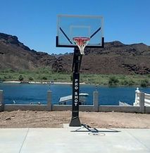 A basketball hoop is sitting next to a body of water with mountains in the background.