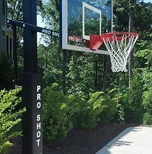 A basketball hoop is sitting on top of a concrete driveway next to trees.