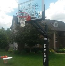 A basketball hoop is sitting in the grass in front of a house.