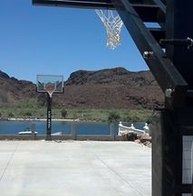 A basketball hoop is sitting on top of a concrete court next to a lake.