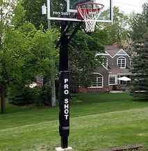 A basketball hoop is sitting in the grass in front of a house.