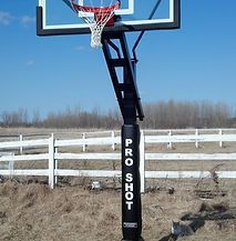 A basketball hoop is sitting in the middle of a field next to a white fence.