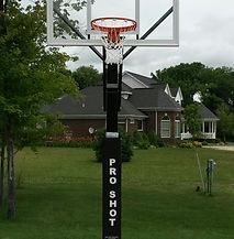 A basketball hoop is sitting in the grass in front of a house.