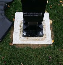 A black pole is sitting on top of a white base in the grass.