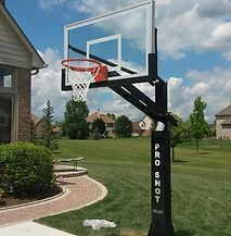A basketball hoop is sitting in the grass in front of a house.