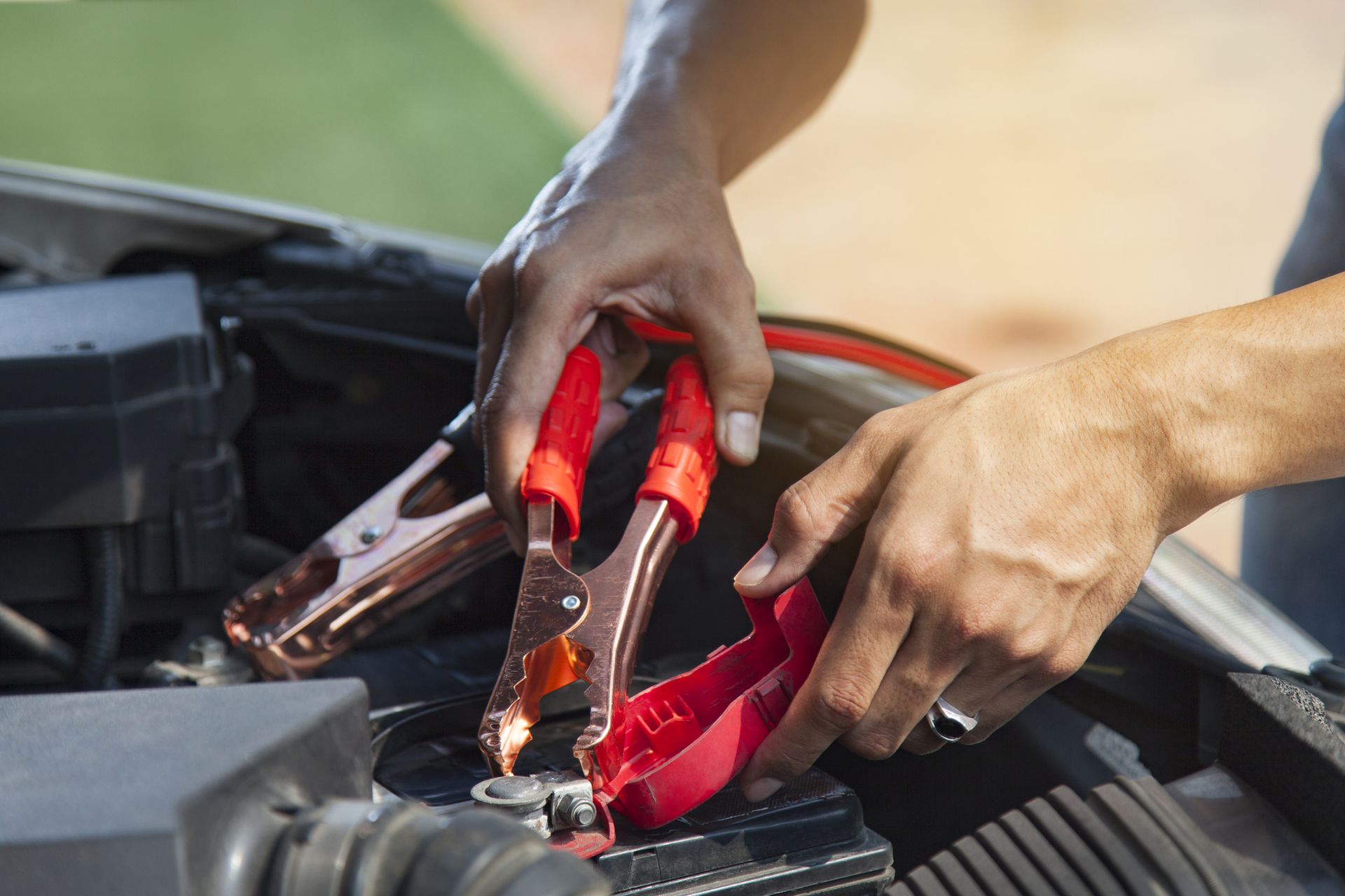 A person is holding a pair of pliers over a car battery.