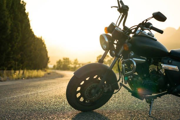 A motorcycle is parked on the side of a road at sunset.