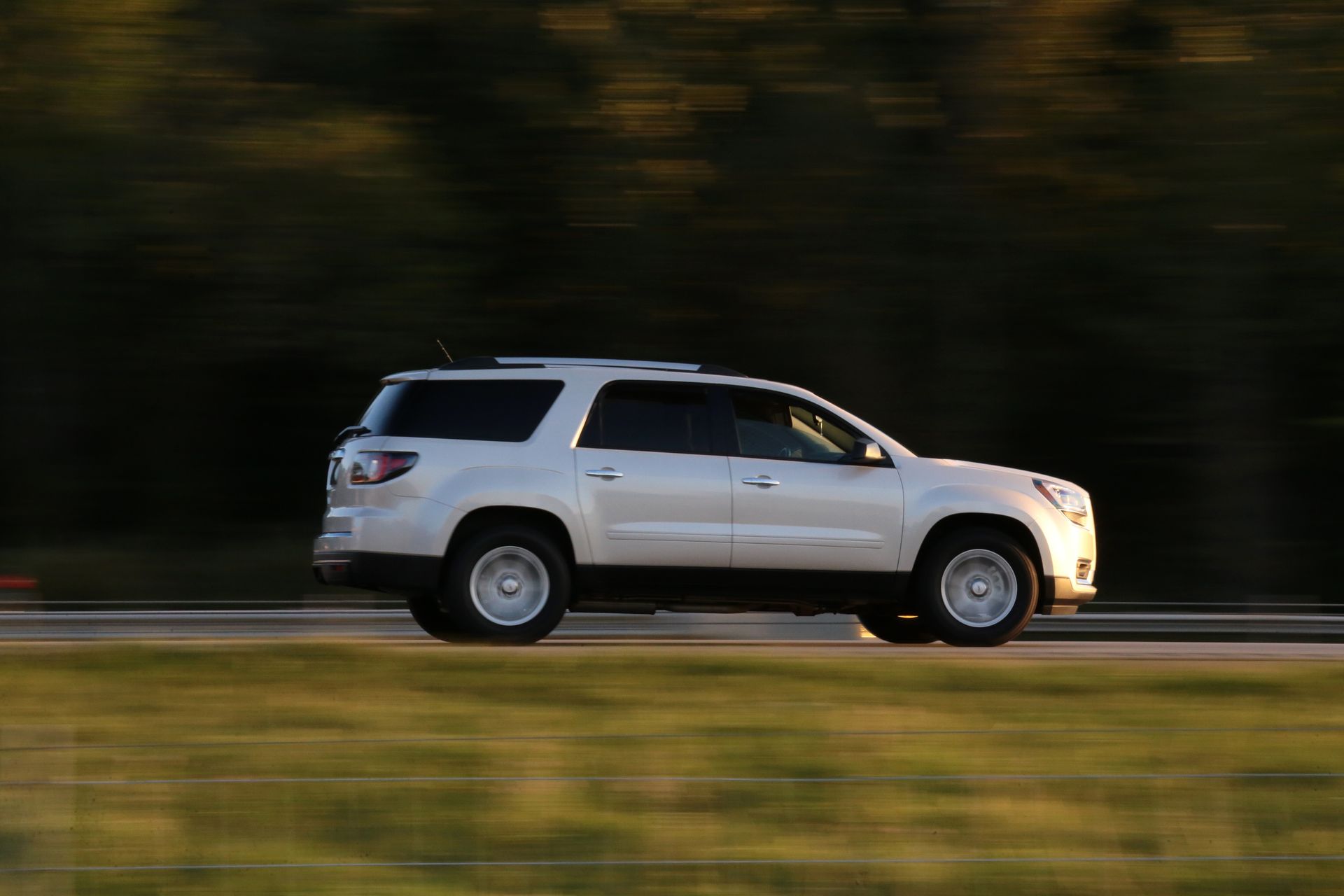 A white suv is driving down a road with trees in the background