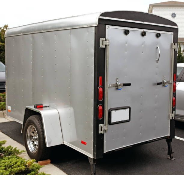 A silver trailer is parked in a parking lot next to a car.