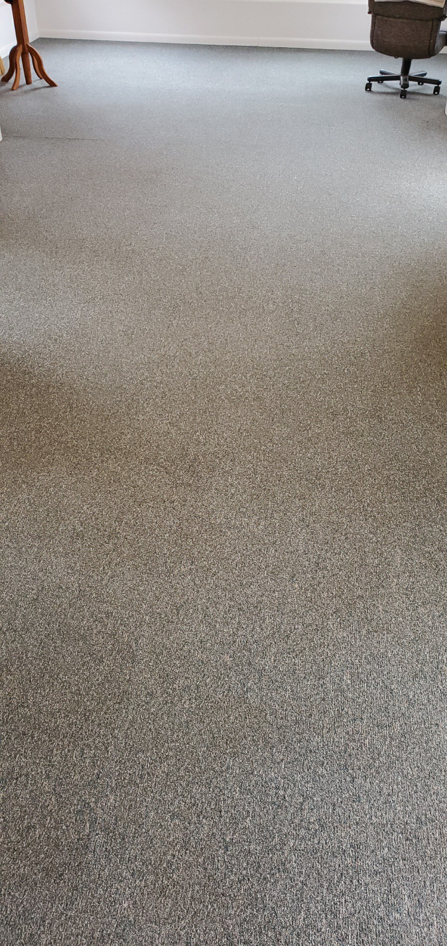 A room with mottled gray carpet, a wooden object, and an office chair.