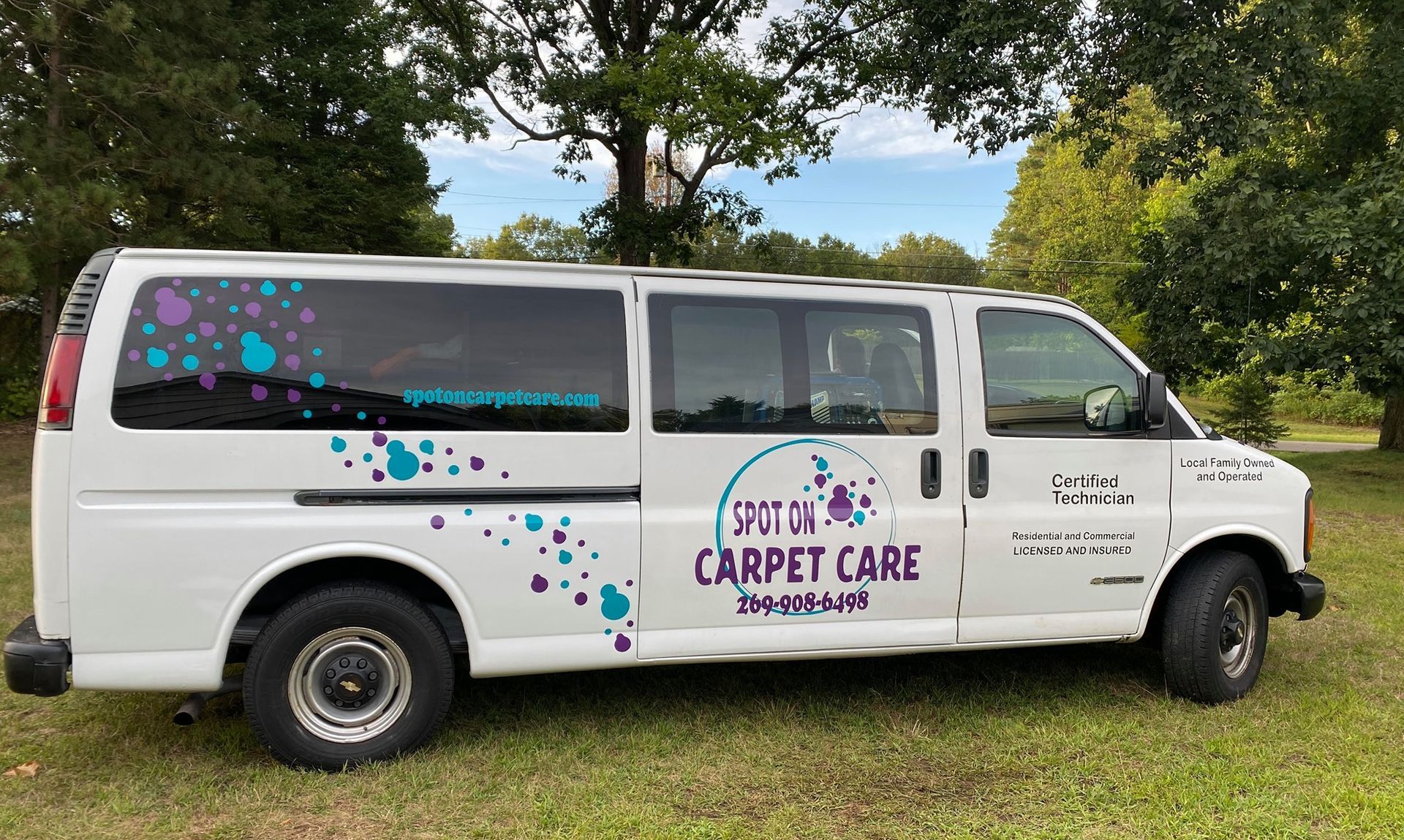 White carpet cleaning van with purple/teal accents on a grassy field.