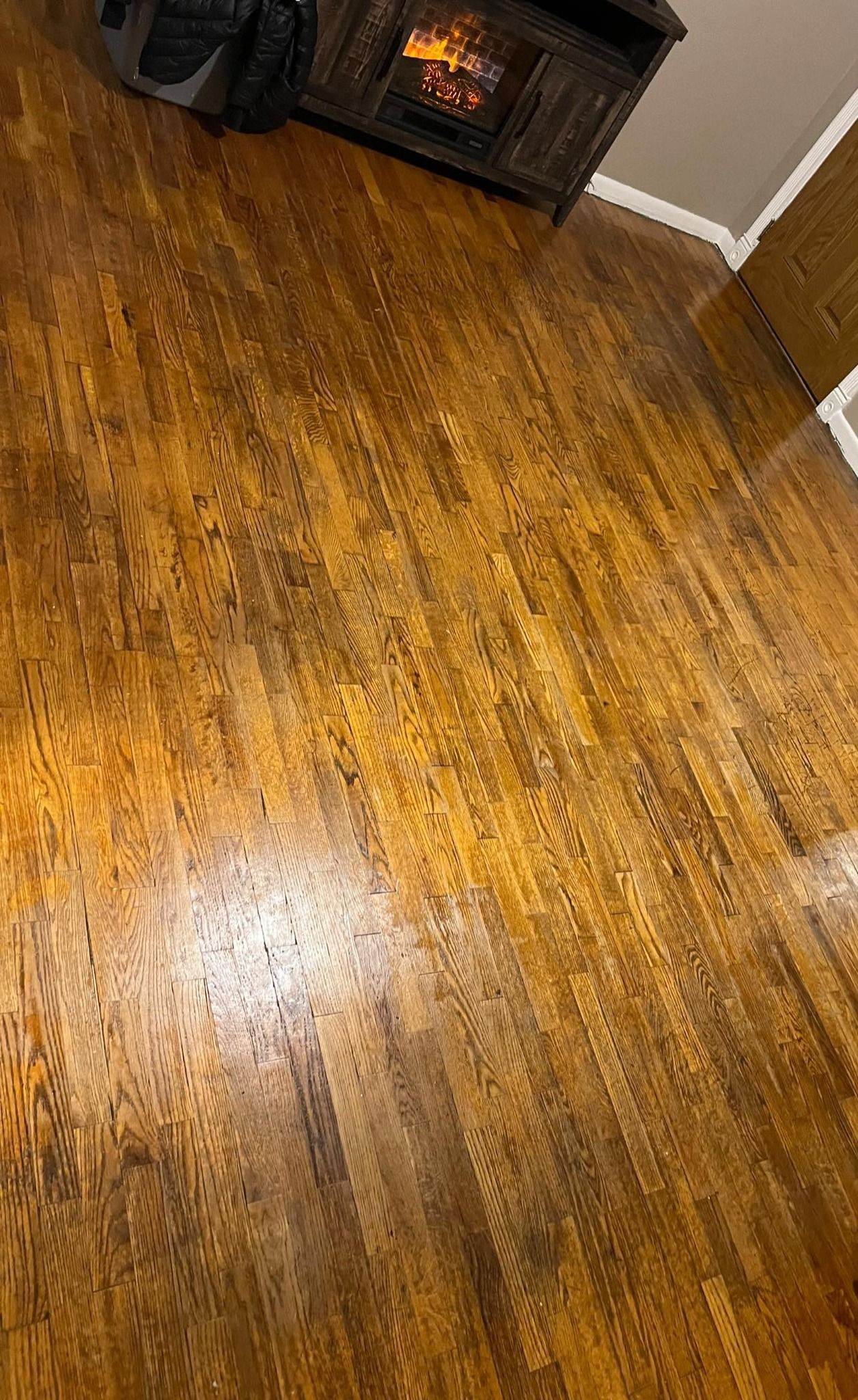 Wooden floorboards with a warm, brown tone, reflecting the light from a fireplace in the top corner.