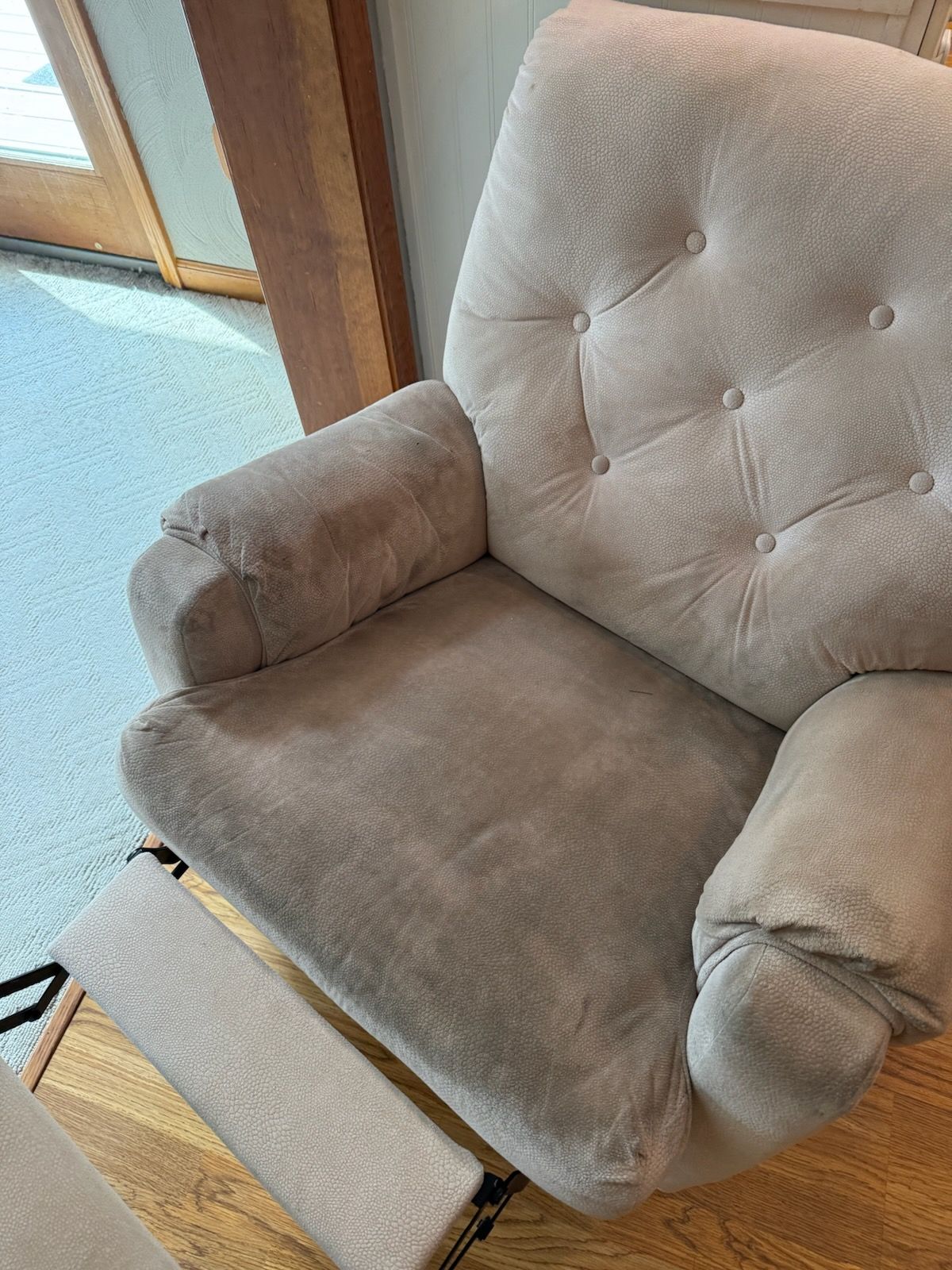 A beige, tufted recliner chair with a footrest in a room with wood flooring.