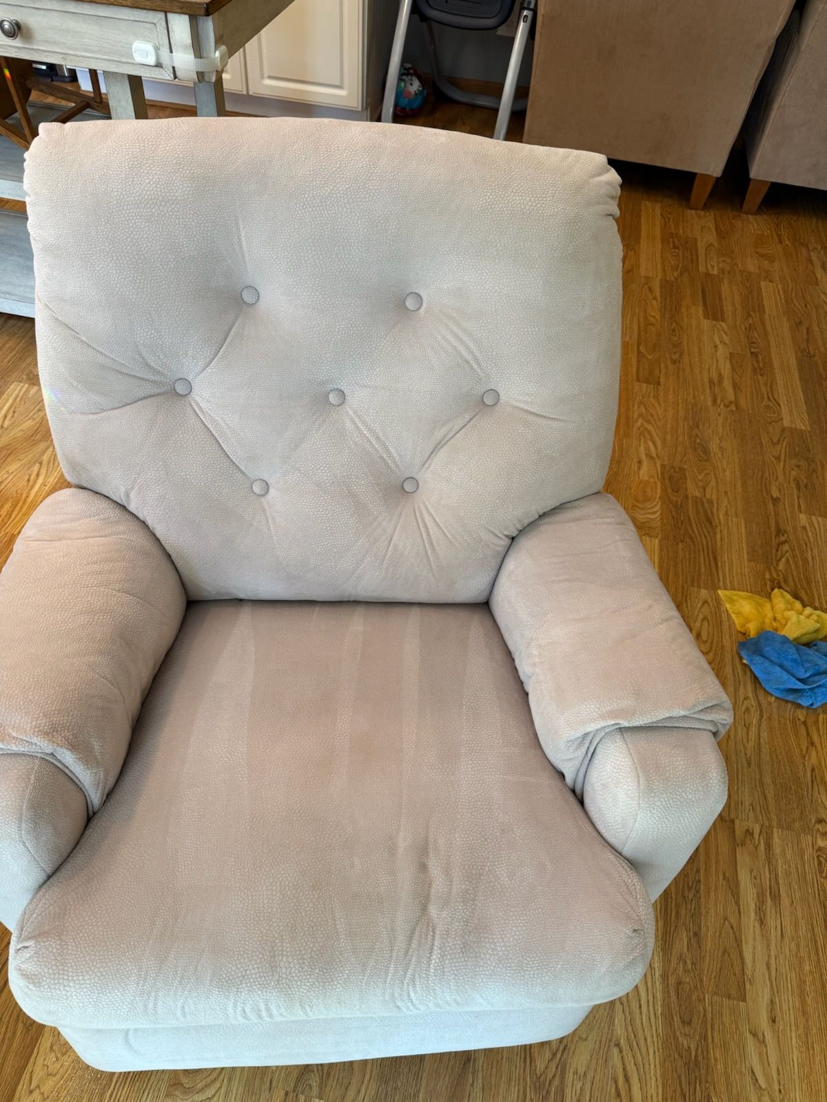 A light beige upholstered armchair with button detailing in a room with wooden flooring.